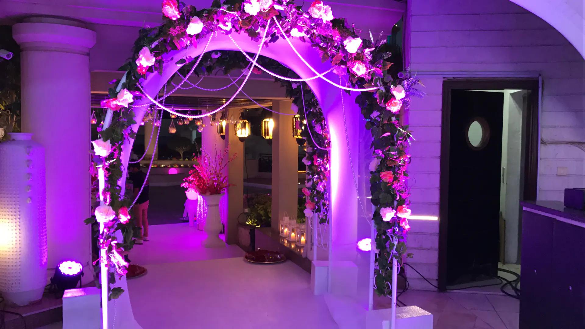 Floral entrance arch illuminated in violet for a private celebration.